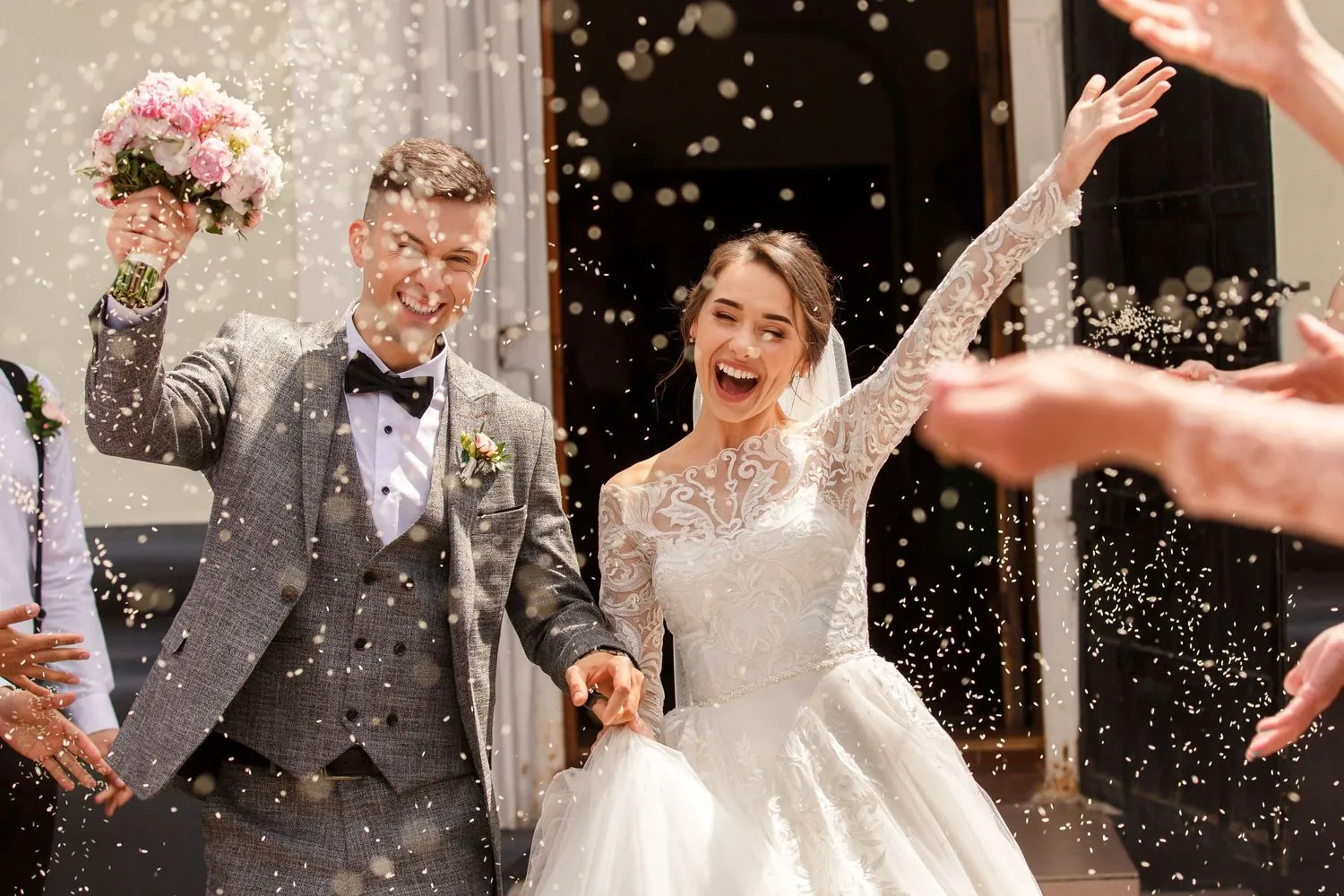 Bride and groom cheering as guests shower them with confetti
