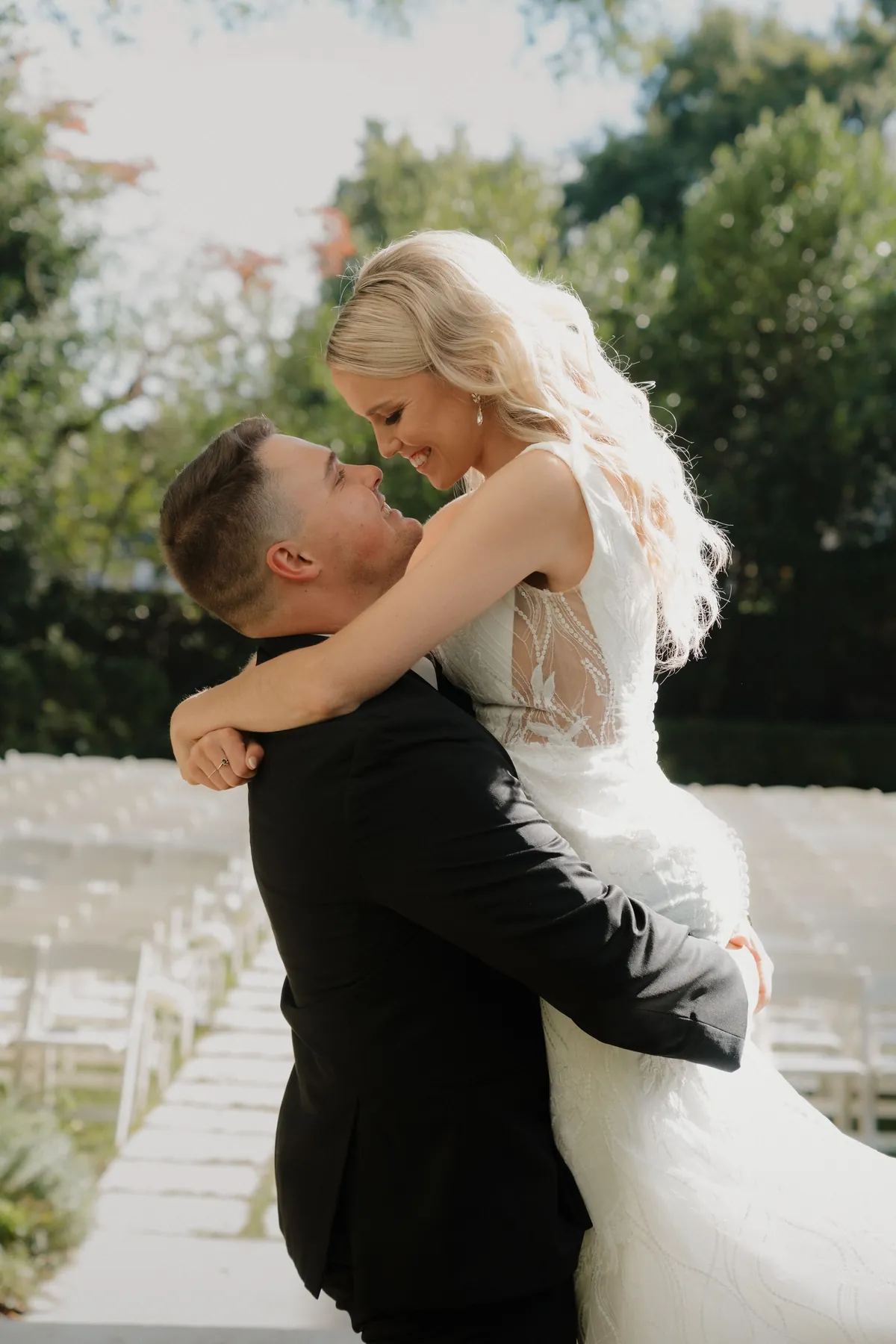 Groom lifting his bride in a hug beside rows of white ceremony chairs