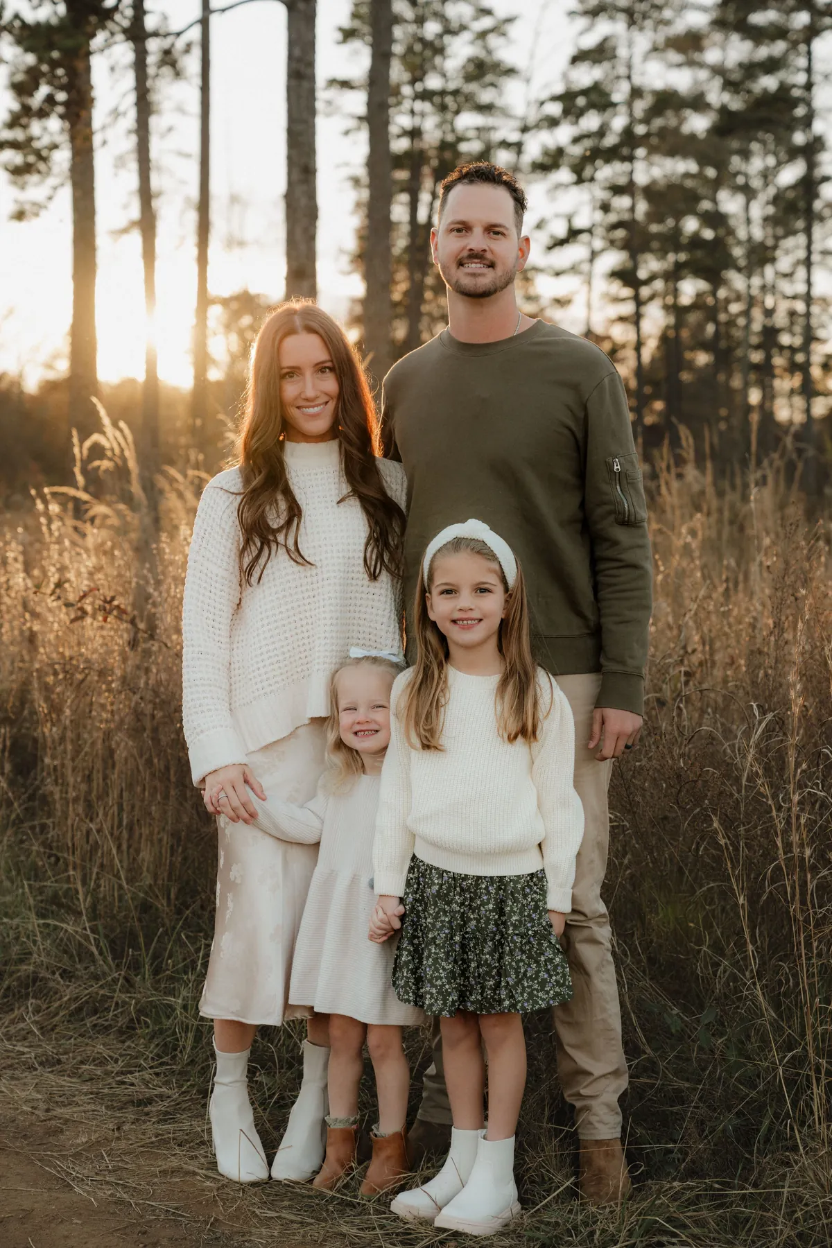 Family of four standing in golden grass among the pines at sunset