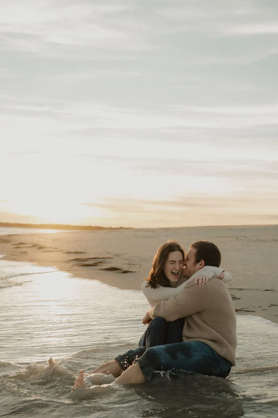 Couple embracing at the water's edge on the beach at sunset