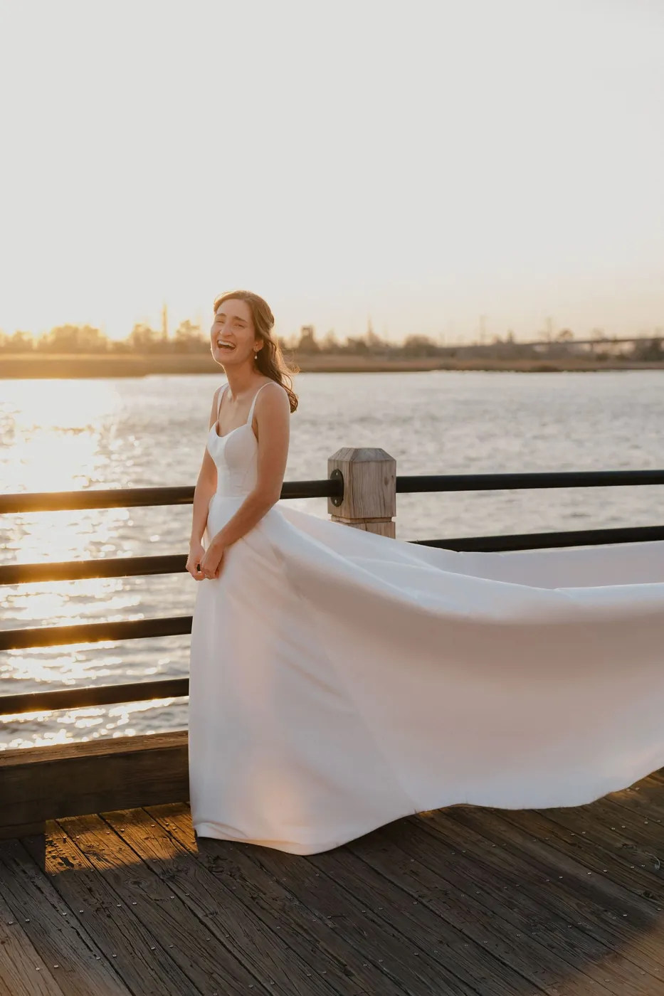 Bride on a waterfront dock at sunset with her train sweeping behind her